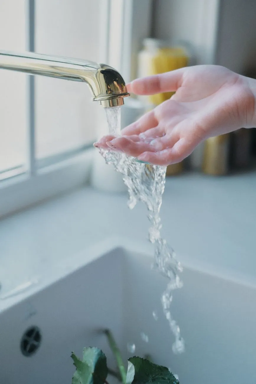 Hand fängt Wasser unter einem goldenen Wasserhahn in einem Waschbecken auf.