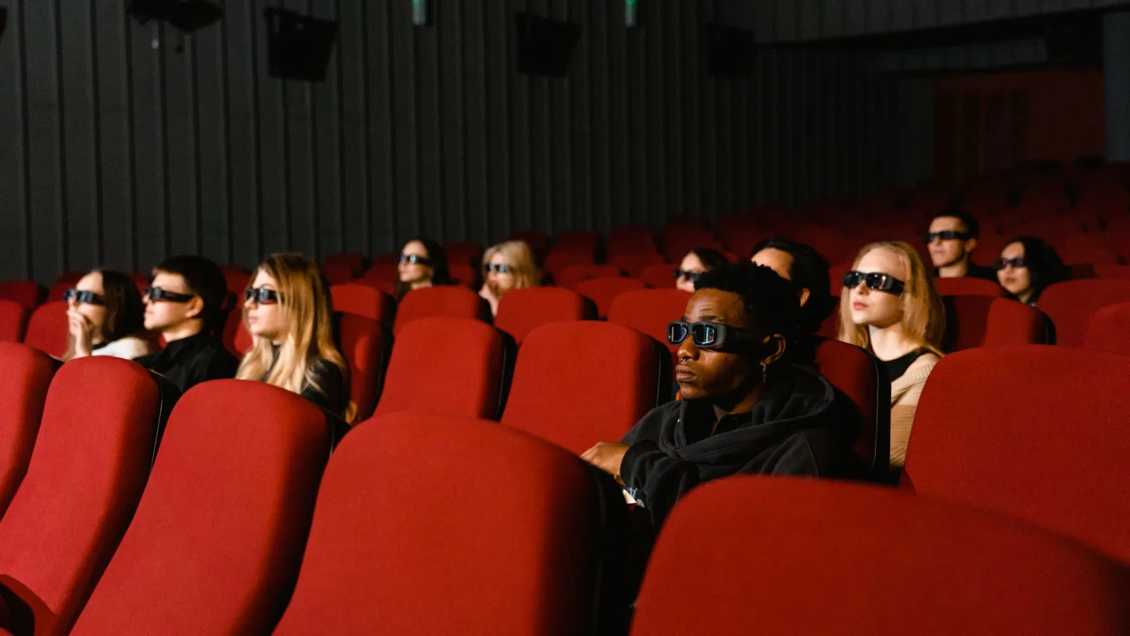 Kino-Besucher mit 3D-Brillen sitzen in roten Kinosesseln und schauen auf die Leinwand.
