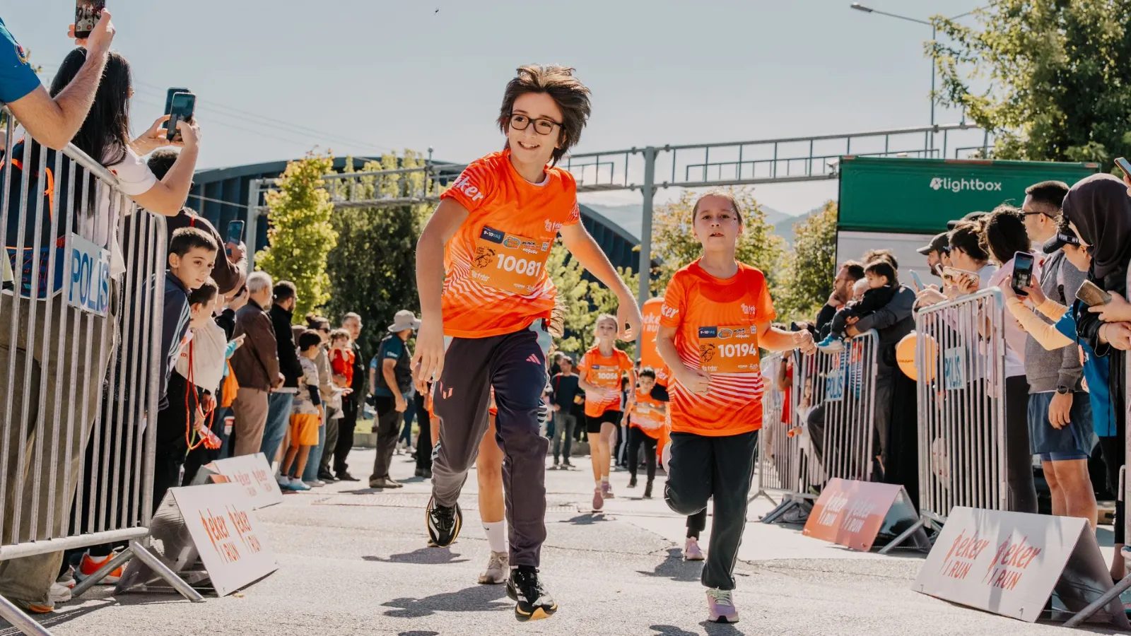 Kinder laufen beim Volkslauf in einem orangefarbenen Trikot mit Startnummern.
