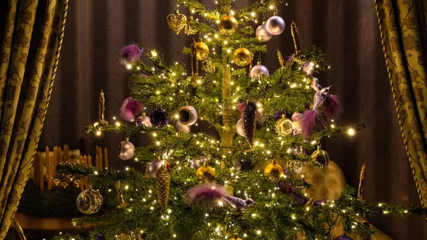 Weihnachtsbaum mit Lichterkette, goldenen und lila Kugeln, sowie Federschmuck
