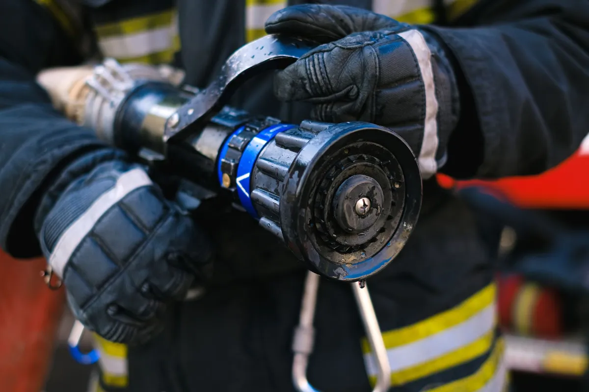 Feuerwehrfrau hält Löschdüse mit blauer Markierung und Sprühkopf aus nächster Nähe, Einsatzkleidung mit reflektierenden Streifen.