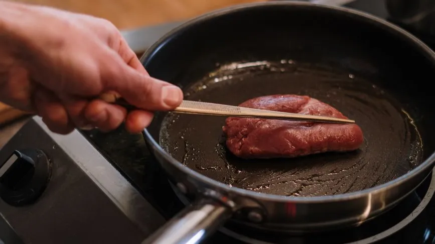 Fleischstück in Pfanne mit Pinzette gebraten