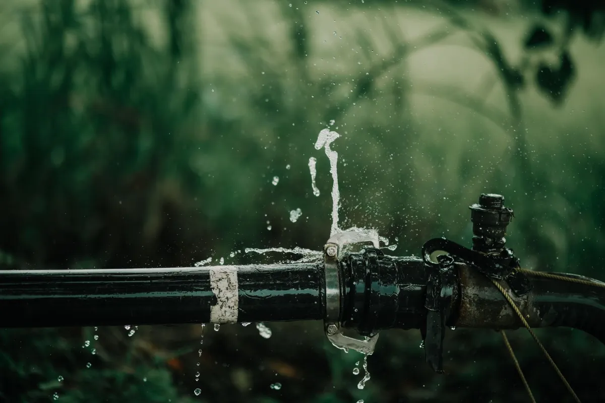 Rohrleitung mit Wasserleck und Spritzern im Grünen.