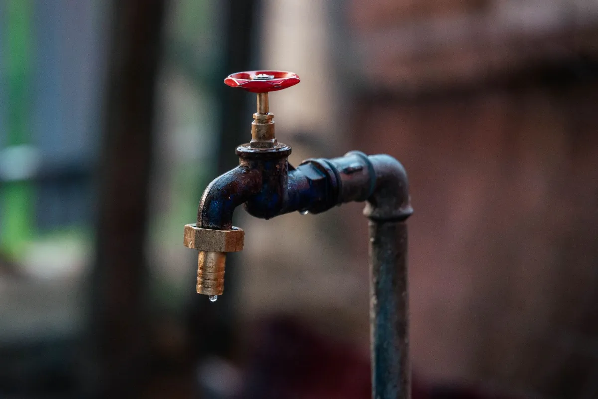 Wasserhahn mit rotem Griff und Tropfen, vor unscharfem Hintergrund