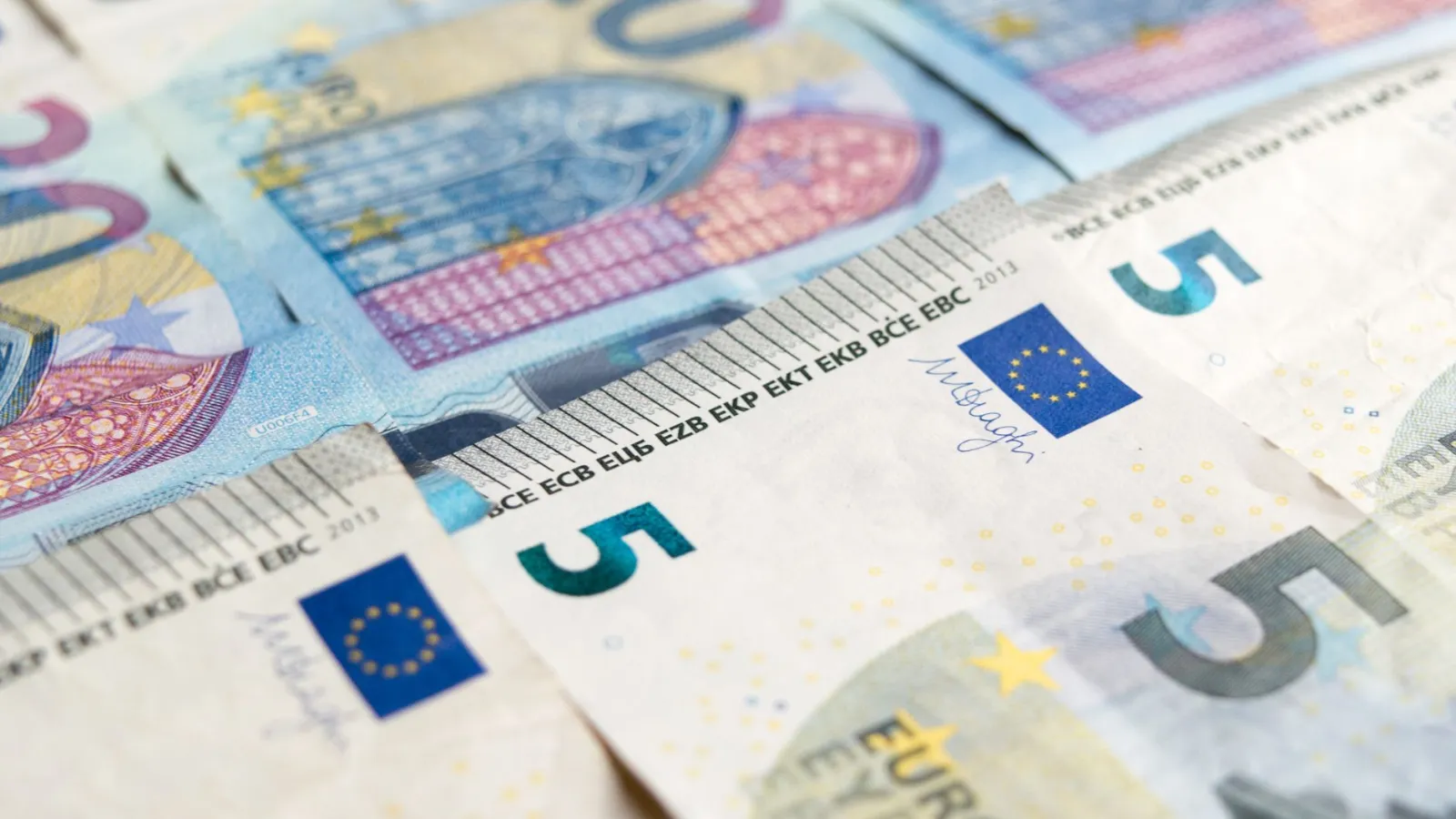 Fünf-Euro-Scheine liegen im Detail nebeneinander, ein blauer Sternenkreis ist zu sehen.