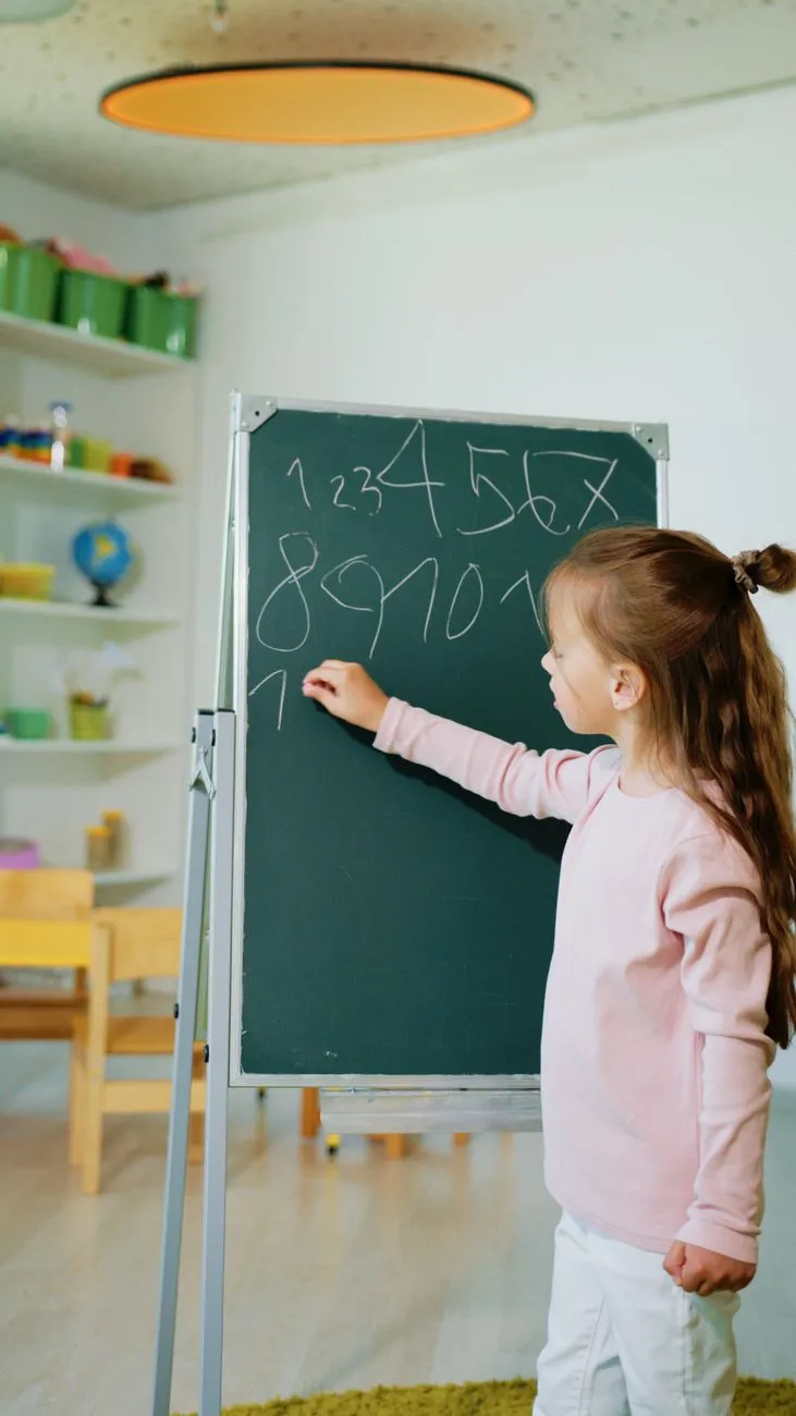 Kind schreibt Zahlen 1 bis 10 auf Tafel in einem hellen Klassenzimmer