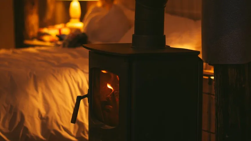 Holzofen mit brennendem Feuer neben einem Bett im Schein einer Lampe
