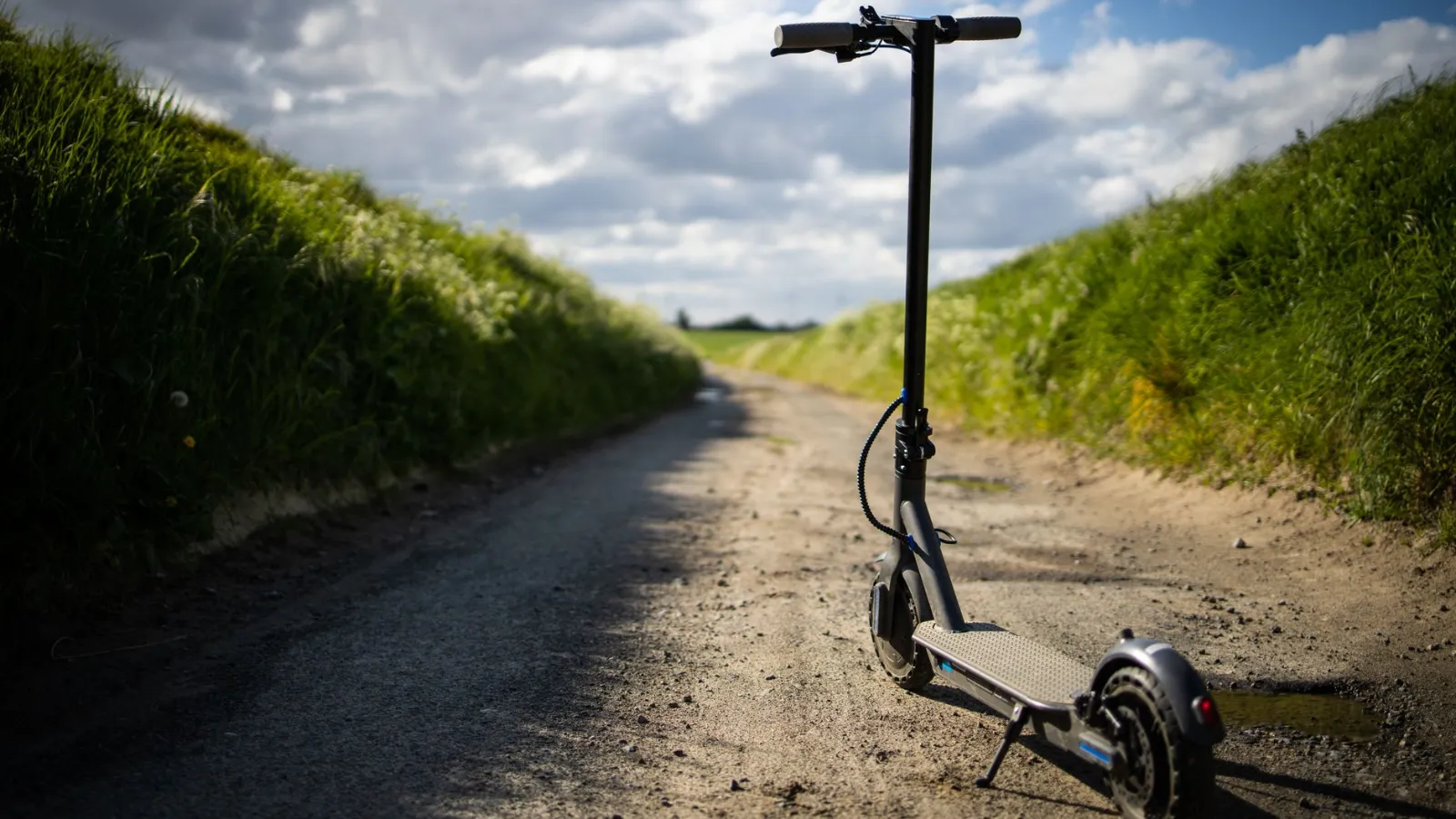 E-Scooter steht auf einem Feldweg mit grasbewachsenen Hängen