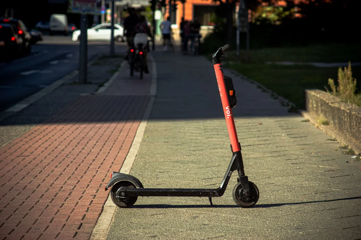 E-Scooter von Voi steht auf einem Gehweg in Wien mit Radfahrern im Hintergrund.