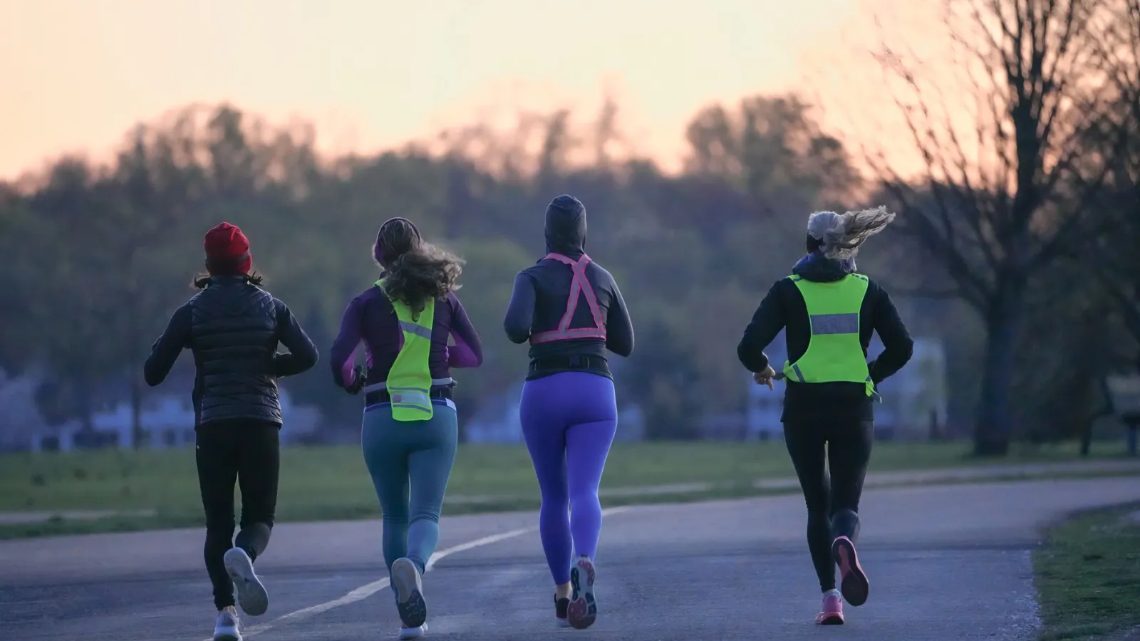 Vier Läuferinnen mit Warnwesten joggen im Park bei Dämmerung