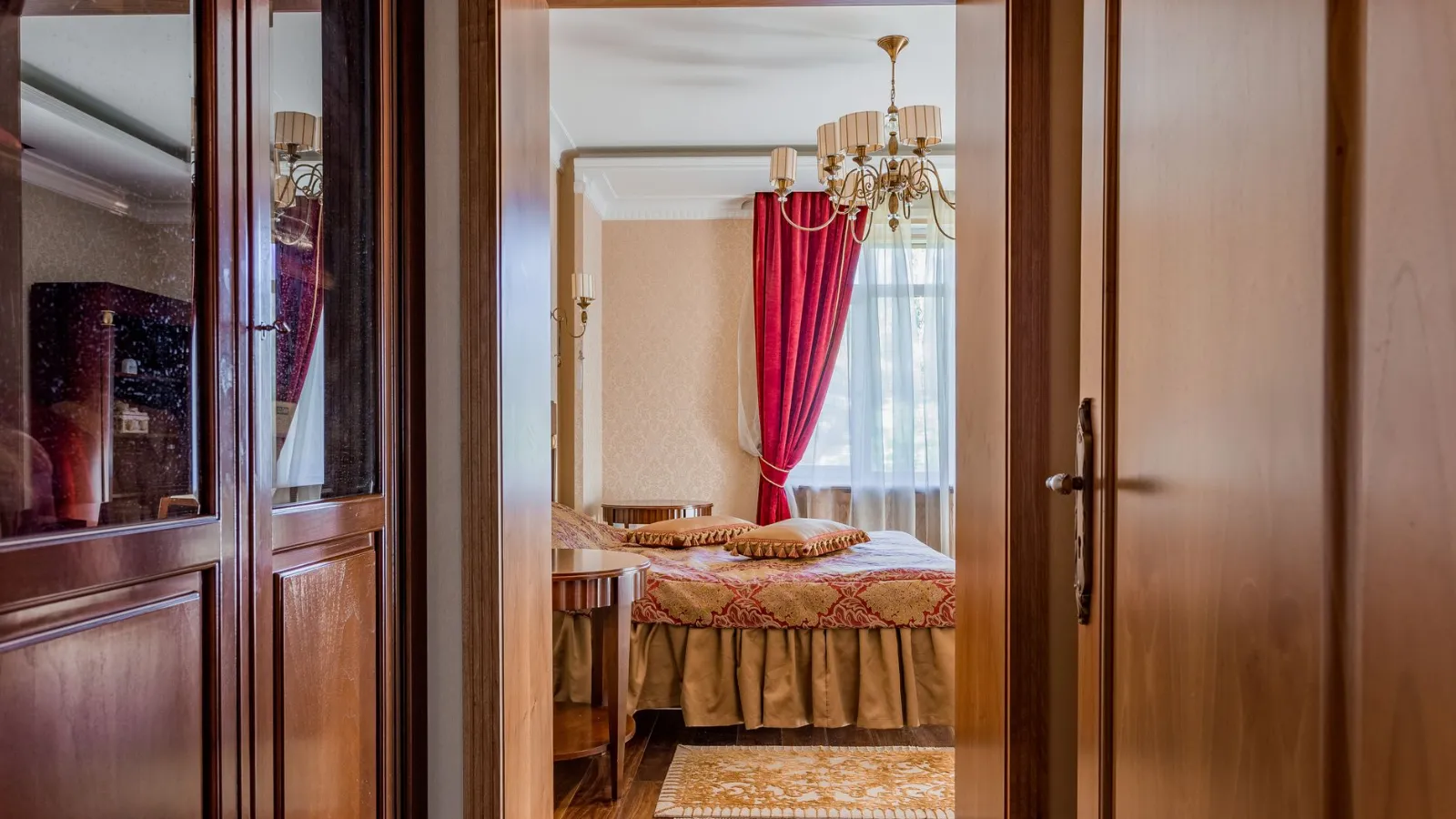 Schlafzimmer mit Doppelbett, roten Vorhängen und Kronleuchter