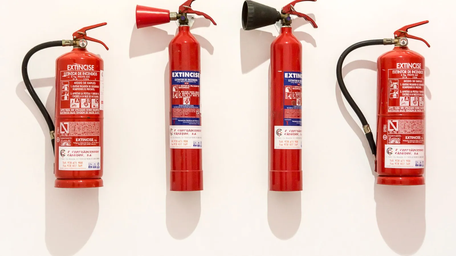 Feuerlöscher rot, vier Stück, an weißer Wand montiert, mit Schattenwurf