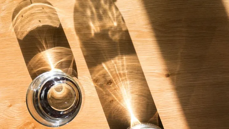 Glas mit Wasser und Lichtreflexionen auf Holztisch