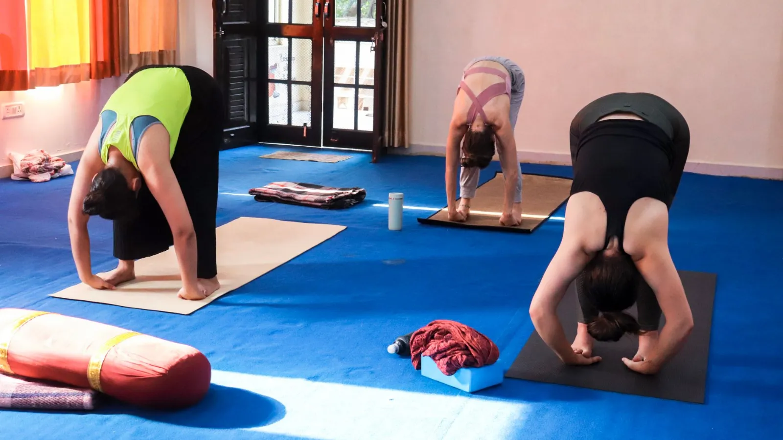Drei Frauen machen Yoga-Übungen auf Matten in einem Raum mit blauem Teppich.