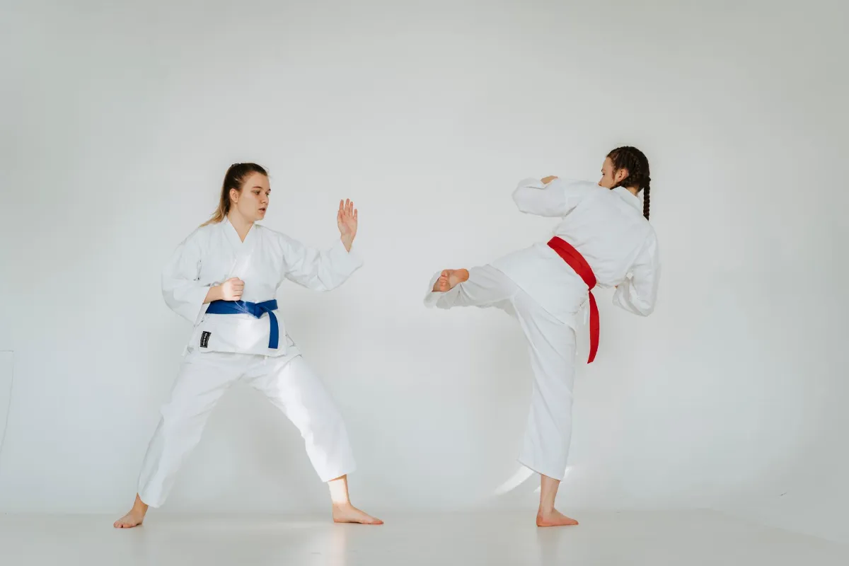 Karate-Training: Zwei Frauen mit blauem und rotem Gürtel üben Tritttechniken im Dojo