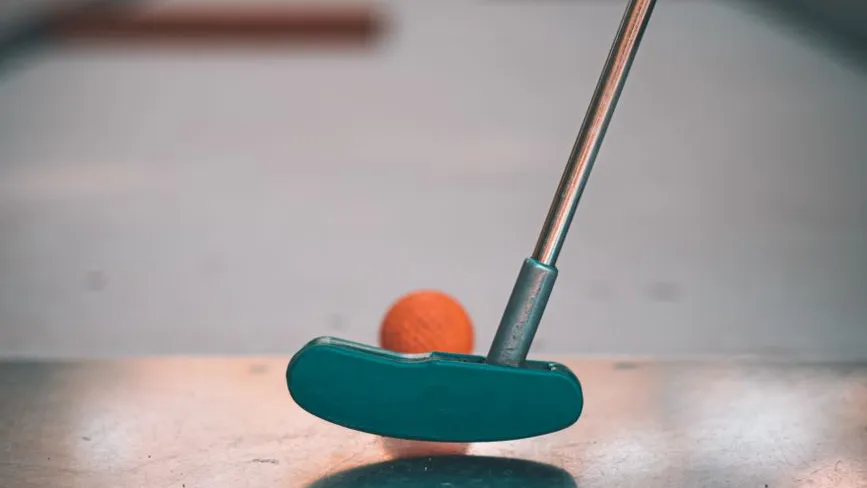 Minigolfschläger mit orangefarbenem Ball auf Tischplatte