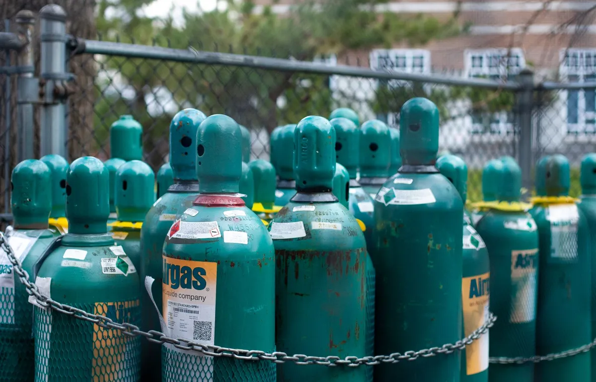 Gasflaschen von Airgas stehen vor einem Zaun und Gebäuden.