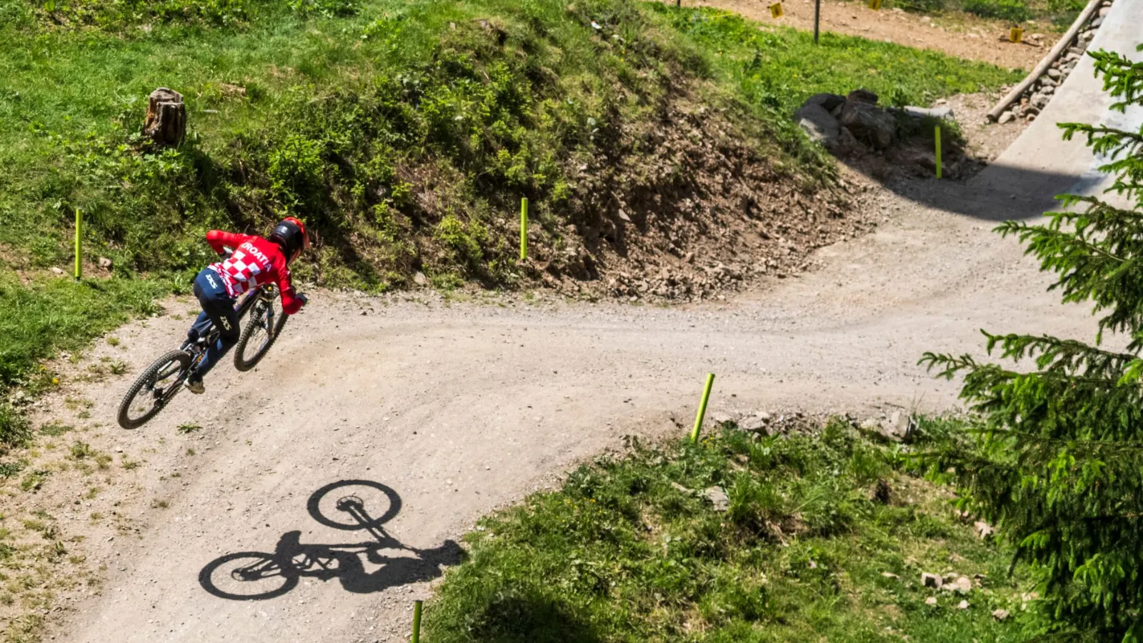 Mountainbikerin mit rot-weiß kariertem Trikot fährt auf Schotterstrecke im Wald