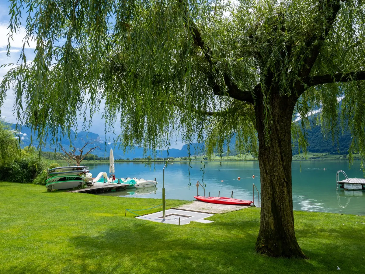 Roter Kajak und Tretboote liegen am Ufer eines Sees mit Bergkulisse.