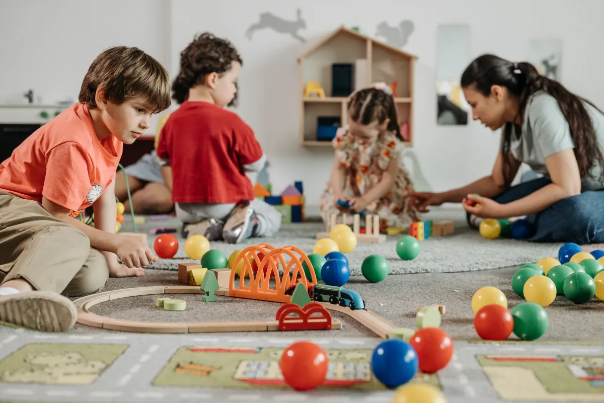 Kinder spielen mit Holzeisenbahn, bunten Bällen und Bausteinen im Gruppenraum