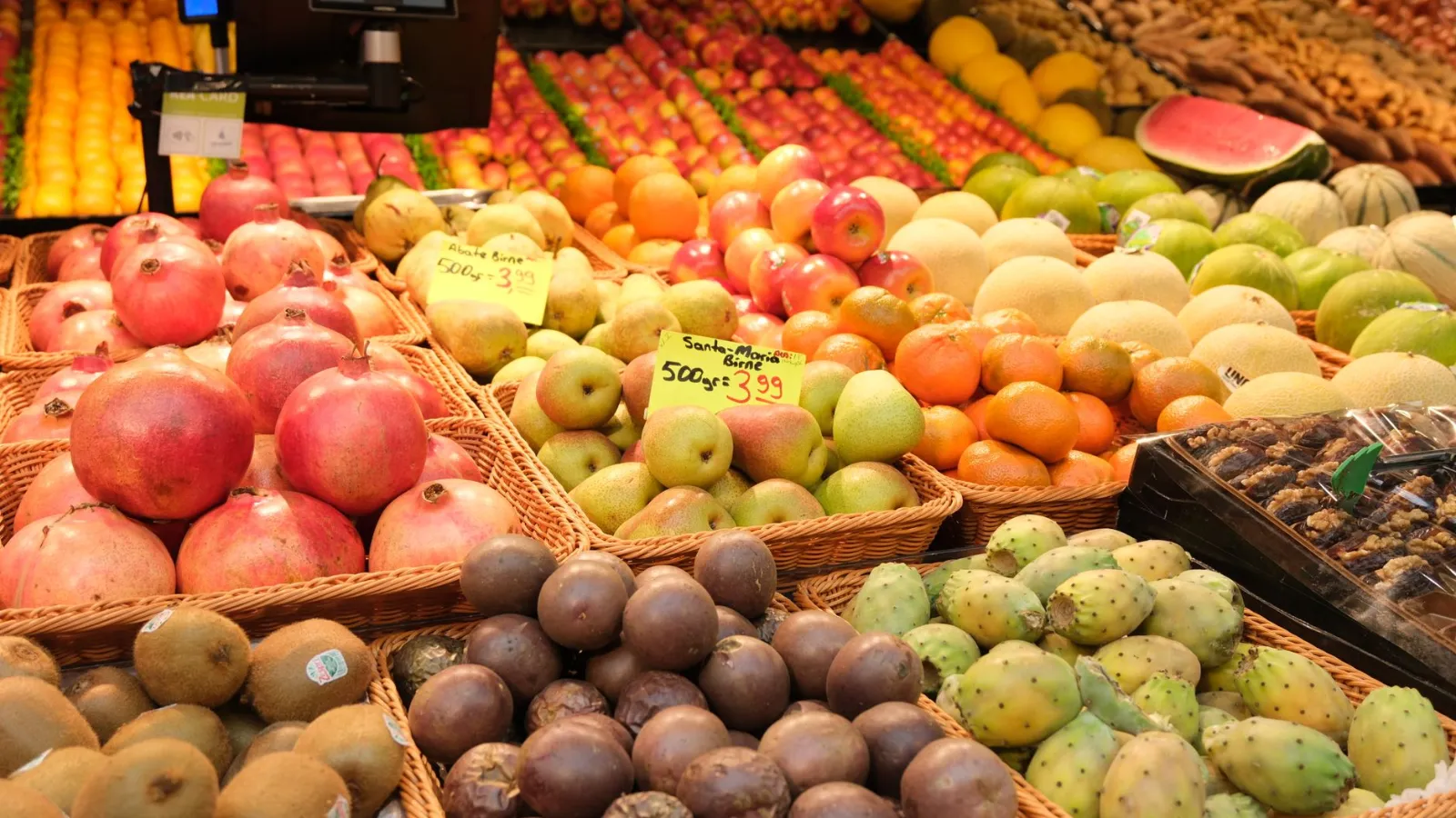 Granatäpfel, Birnen und Kiwis in Körben auf einem Marktstand mit Obstauslage