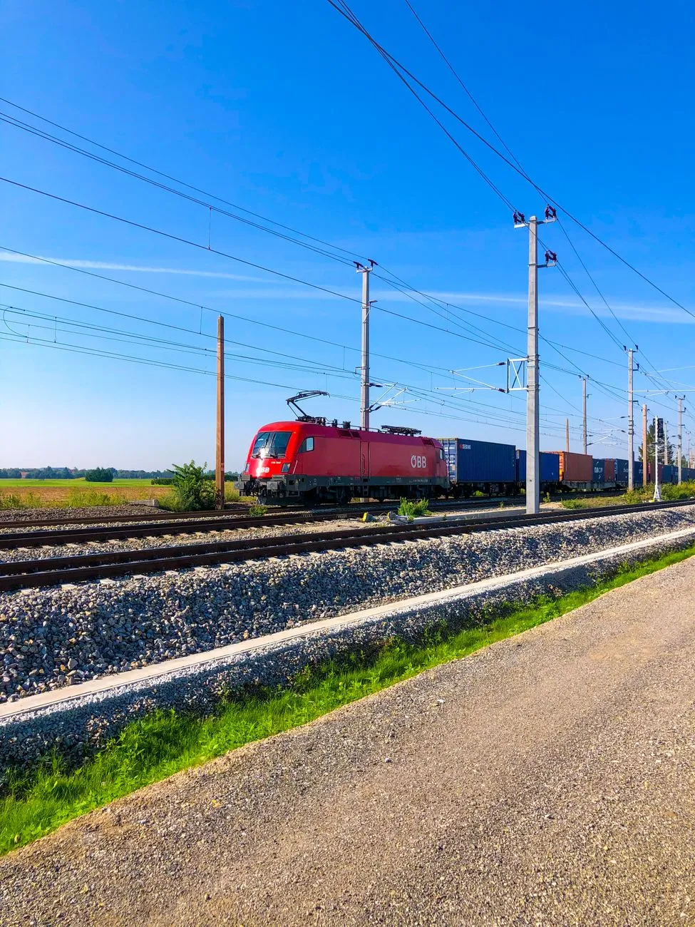 ÖBB-Lokomotive zieht Güterwaggons auf Gleisen in Österreich unter blauem Himmel
