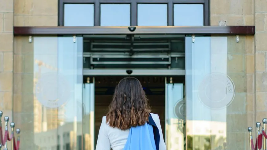 Frau mit dunklem Haar betritt durch Glastüren ein Gebäude in Wien.