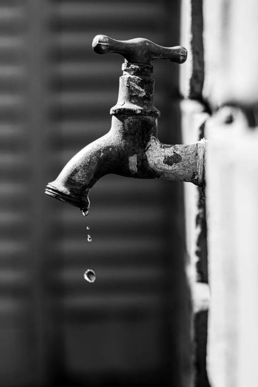 Tropfender Wasserhahn vor Ziegelmauer